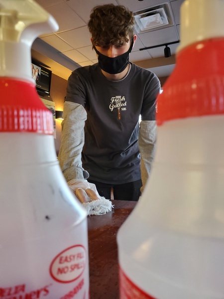 Austin Monroe sanitizes tables in between guests at his part-time job.  The extra safety protocols have increased the work load and stress for many high school workers. 